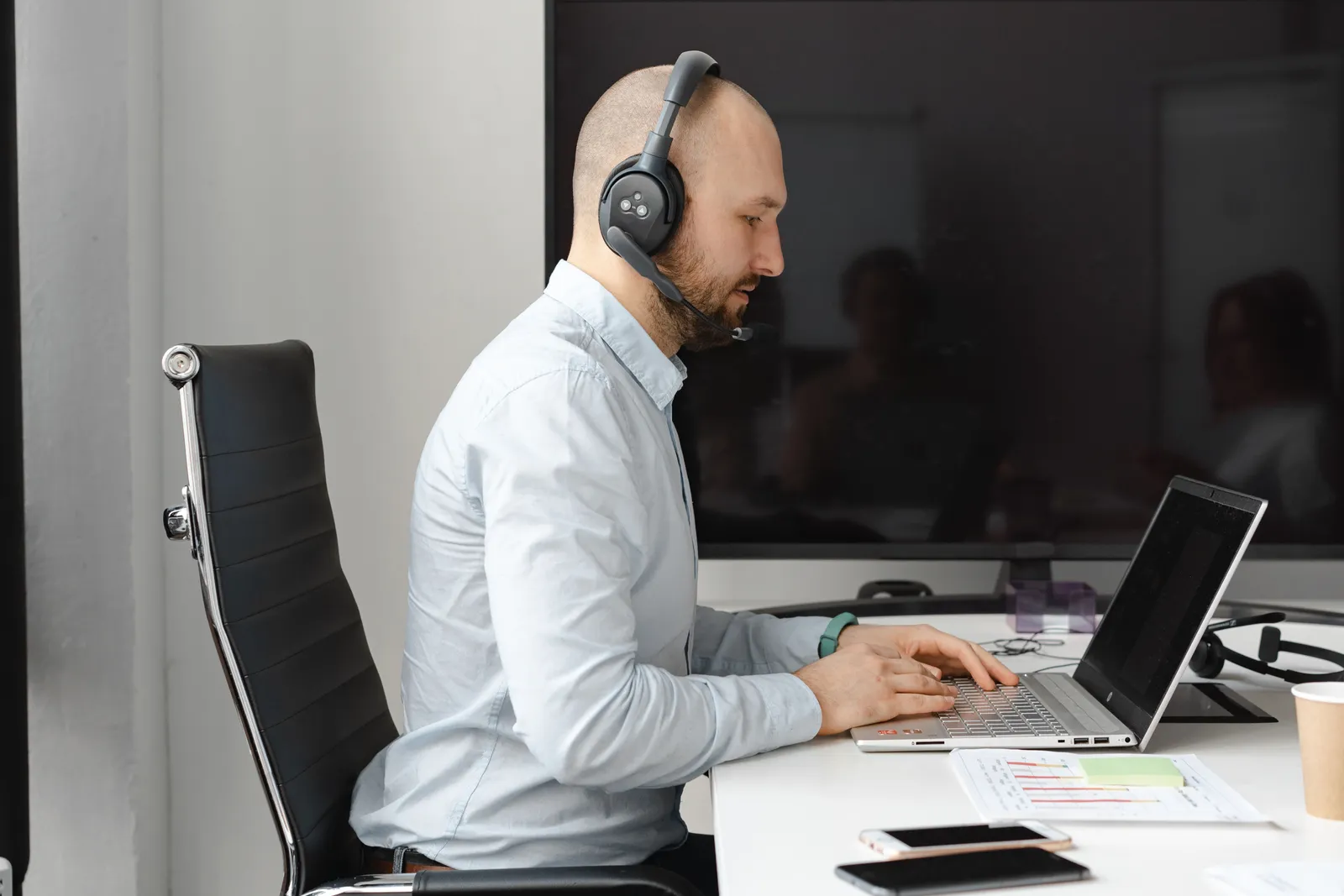 A focused call center agent with headphones working on a laptop in an office