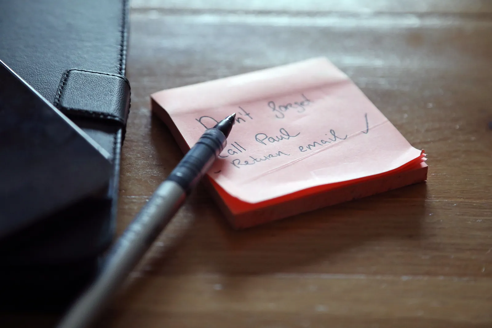 A close-up of sticky notes with a to-do list, a pen, and a wallet on a wooden desk