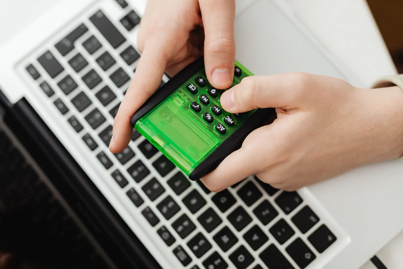 Hands using a green calculator on a laptop keyboard, representing business and finance tasks