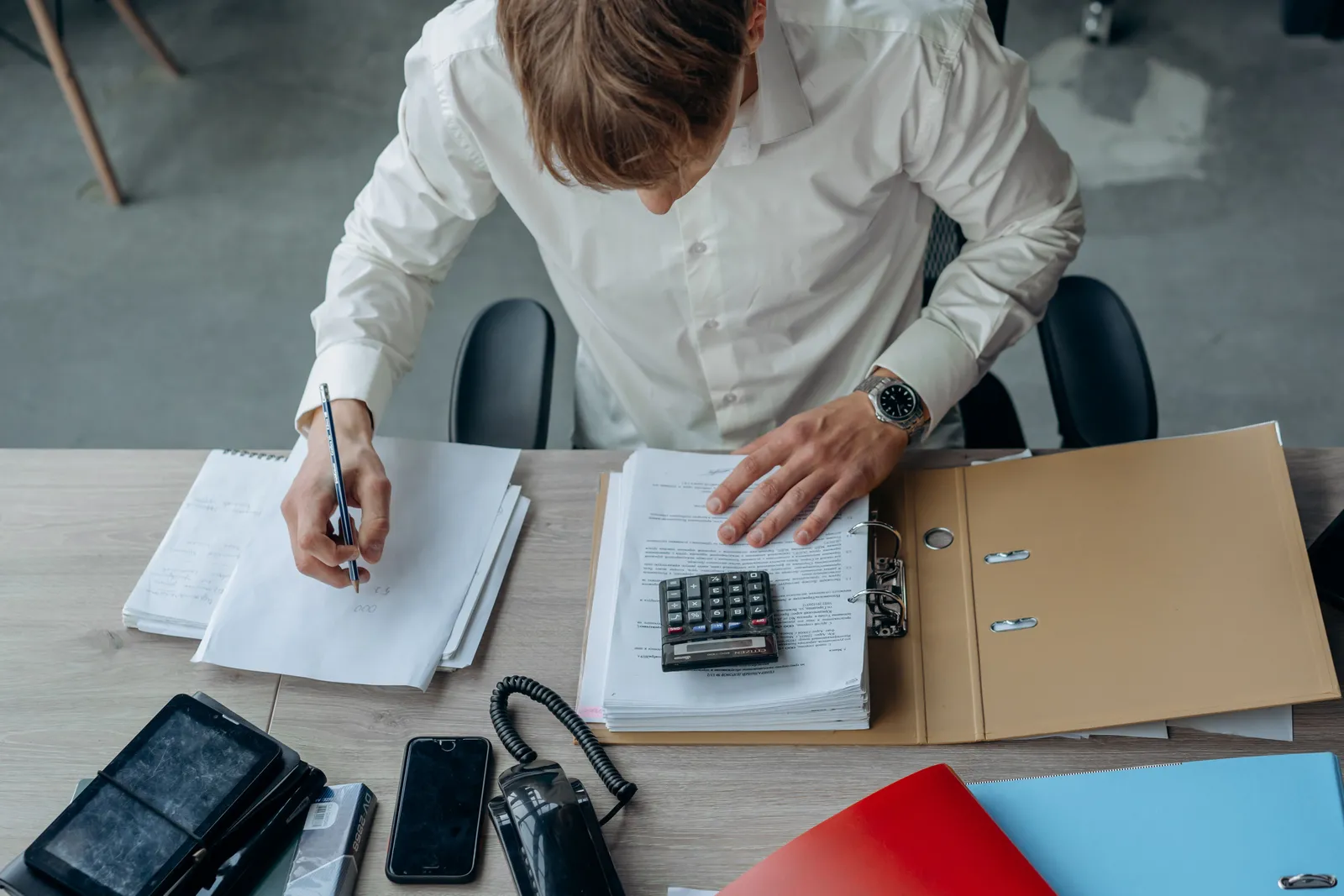 Man in an office reviewing financial papers with a calculator on a desk