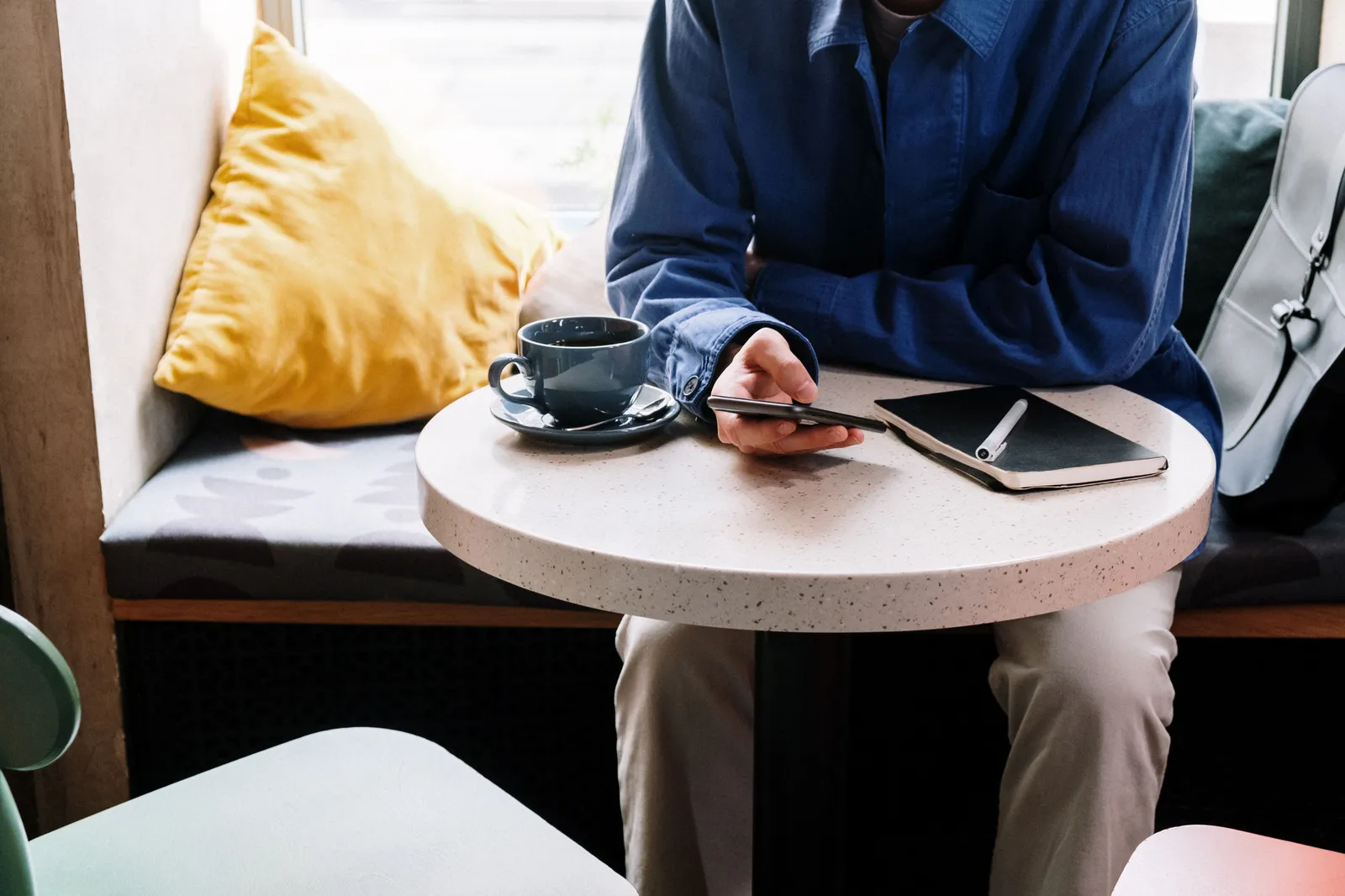 Person in blue shirt using smartphone at cafe with coffee and notepad