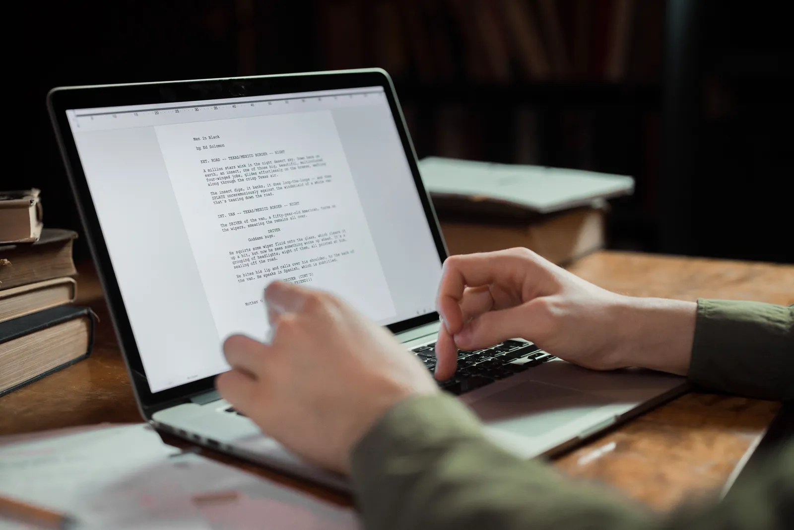 A person typing on a laptop in a cozy workspace with books around. Perfect for writing and technology themes