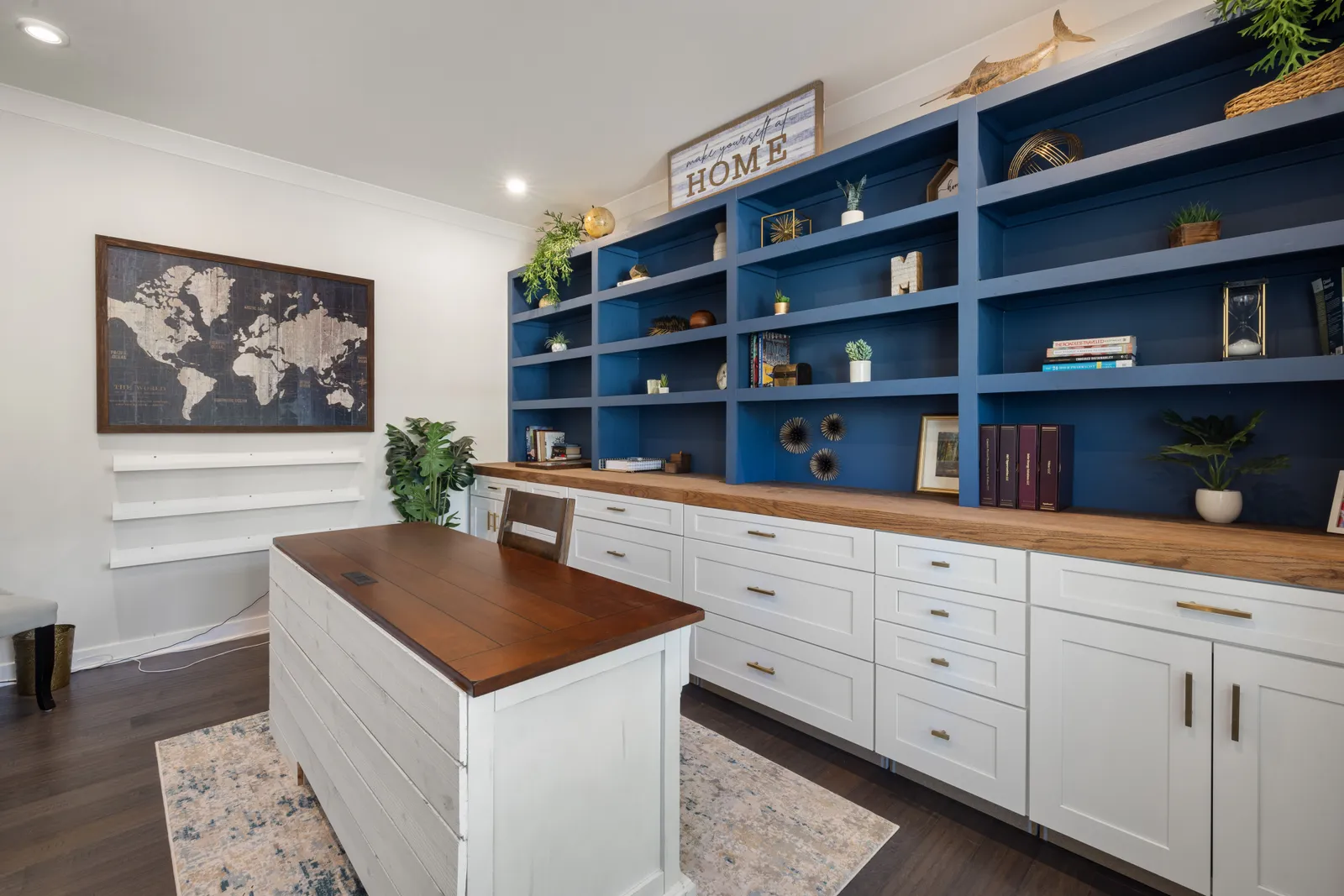 Modern home office featuring blue shelves with decor, a wooden desk, and world map artwork