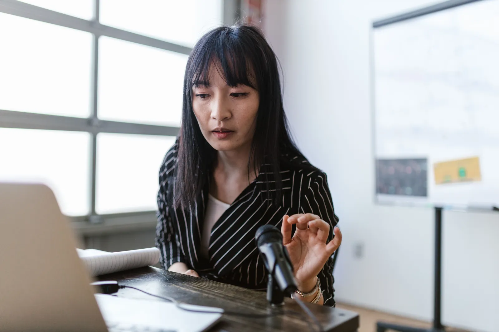 Woman in office presenting at a desk with a microphone, wearing striped shirt