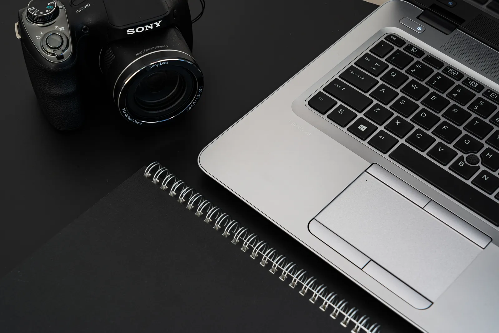 A stylish office desk featuring a laptop, camera, and spiral notebook on a dark surface