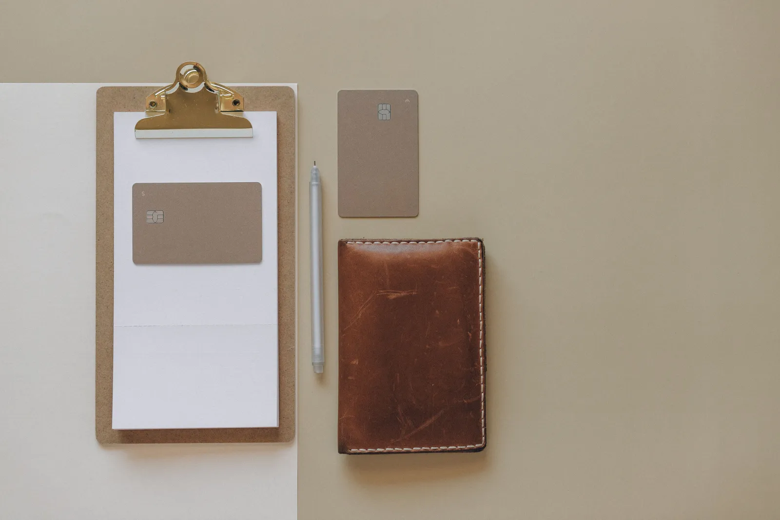 Flat lay of a minimalist office desk with clipboard, credit cards, pen, and leather wallet
