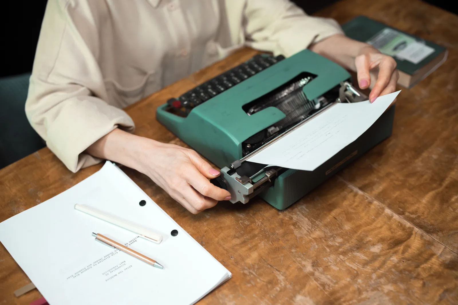 Close-up of hands using a vintage typewriter, with paper and script on a wooden desk