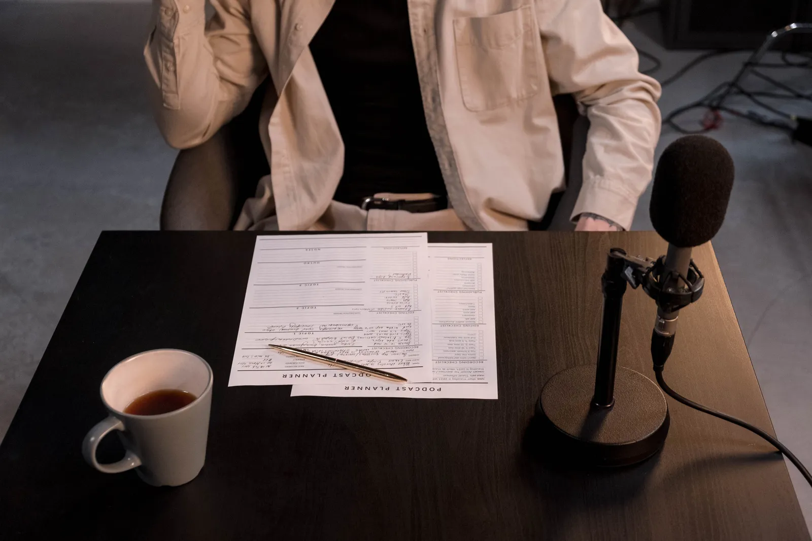 A podcast setup with microphone, papers, and coffee cup on a desk