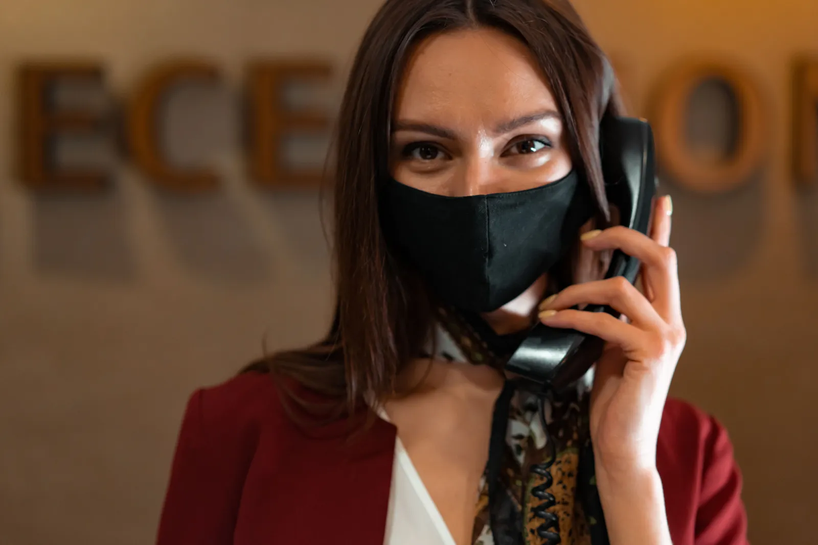 Professional woman receptionist wearing a mask while talking on the phone at the reception desk