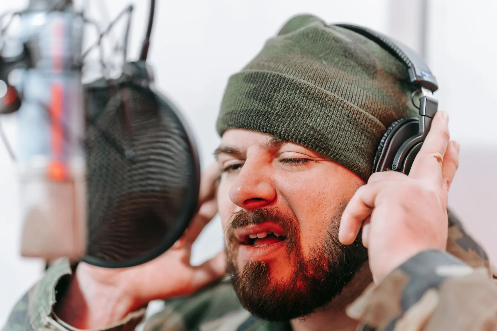 Close-up of a musician recording vocals in a studio, wearing headphones and camouflage