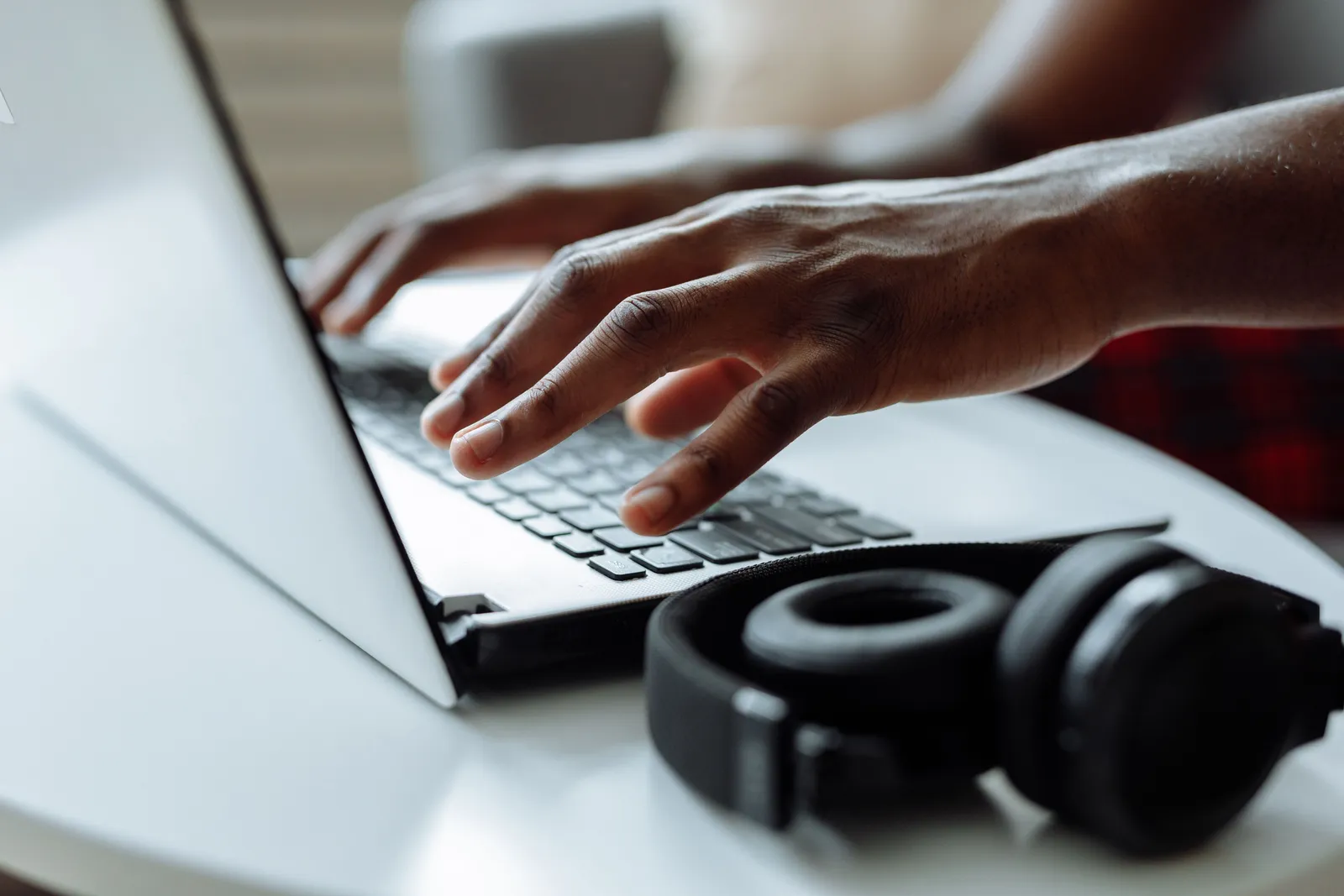 A person typing on a laptop with headphones on a table, ideal for remote work concepts