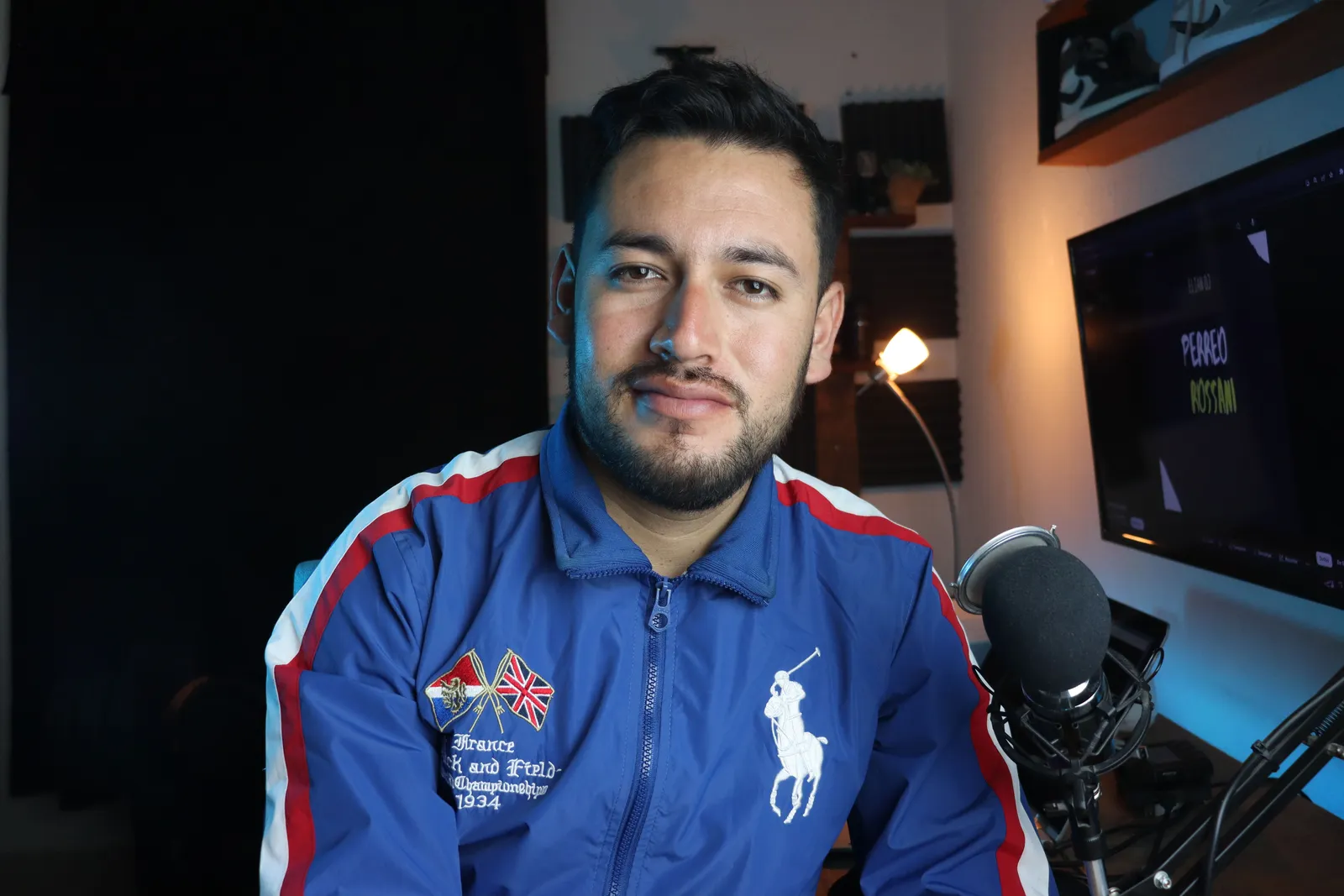 Man in a blue jacket with microphone recording a podcast in a home studio setup
