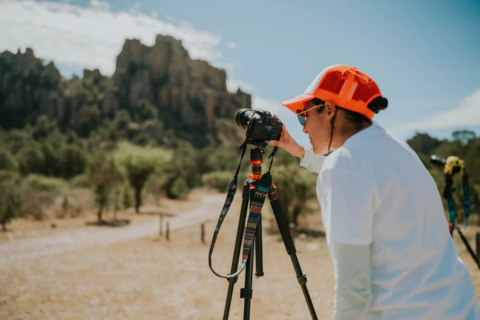 A woman uses a digital camera on a tripod to photograph a stunning outdoor landscape