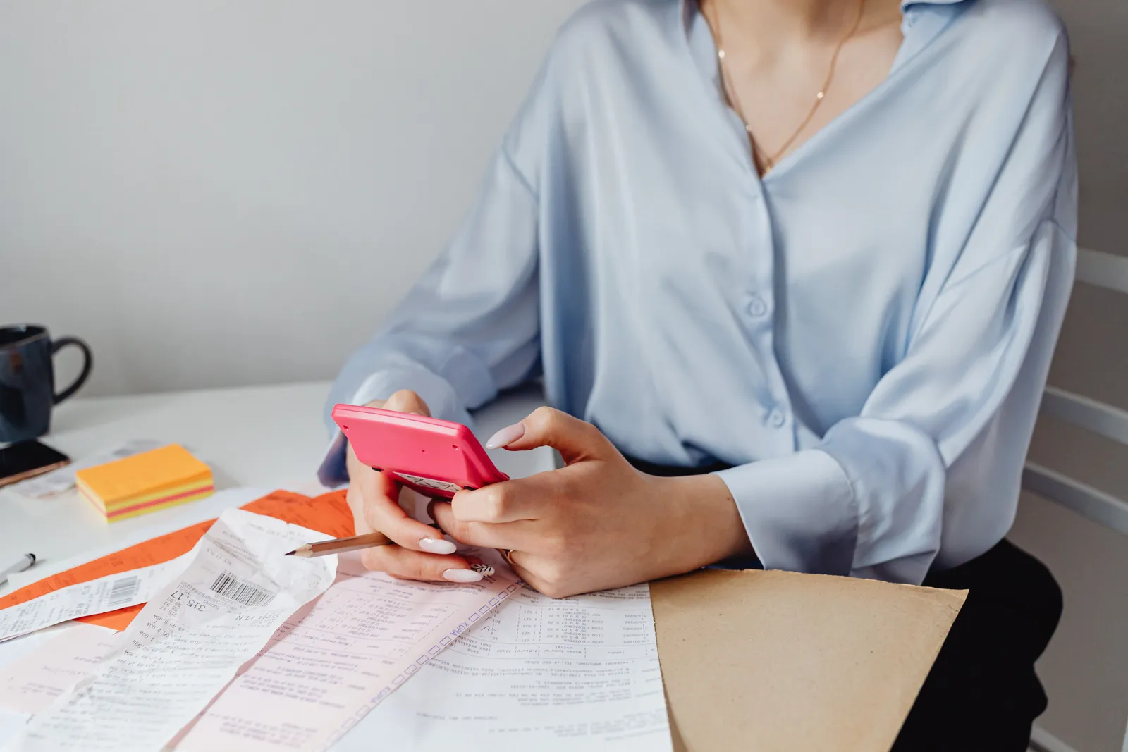 A woman using a pink calculator surrounded by bills and receipts at a desk