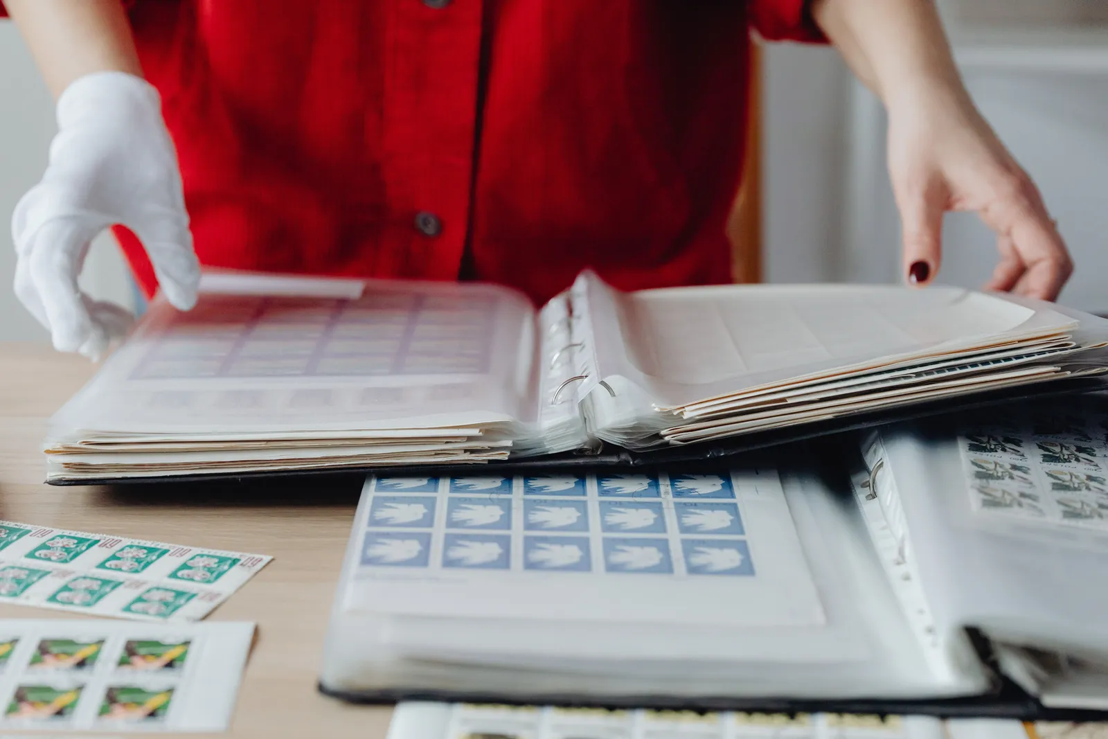 Person in red sorting a collection of vintage postage stamps using gloved hands on a wooden table