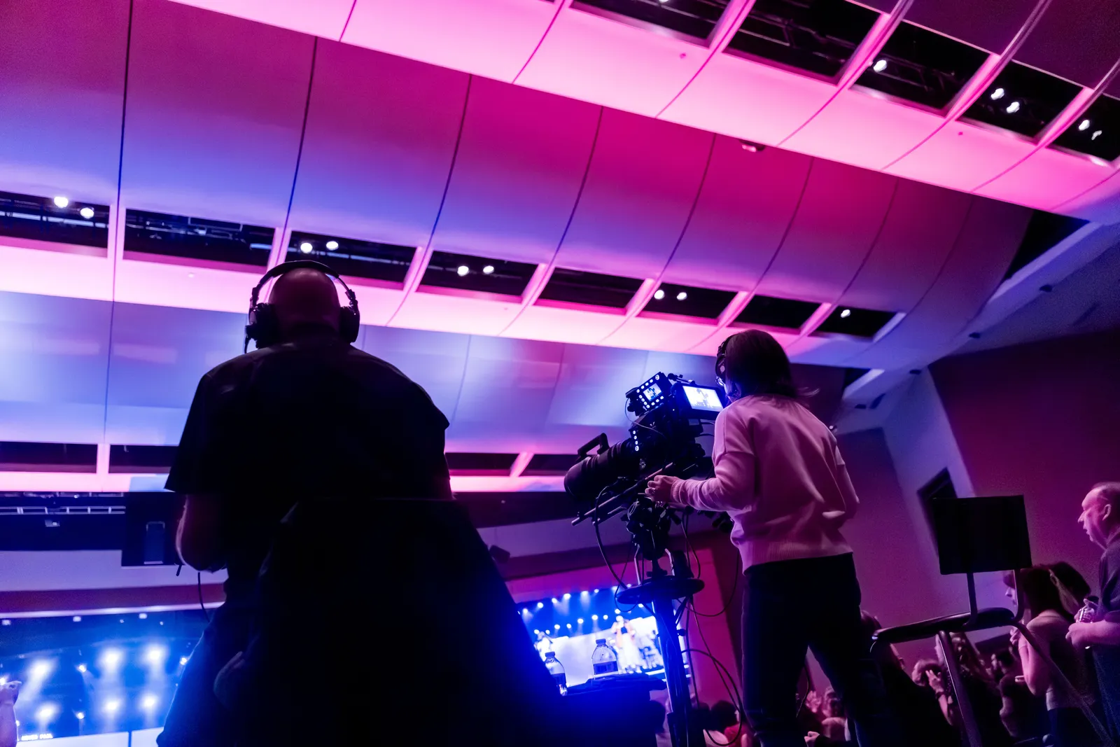 Professional camera crew filming a live event indoors, capturing vibrant stage lighting