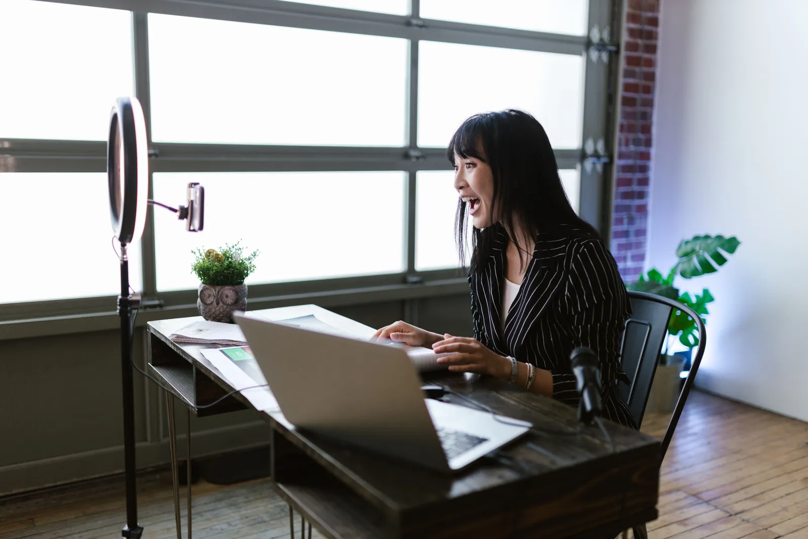 Woman in office setting recording content with laptop and ring light, showcasing elegant business setup
