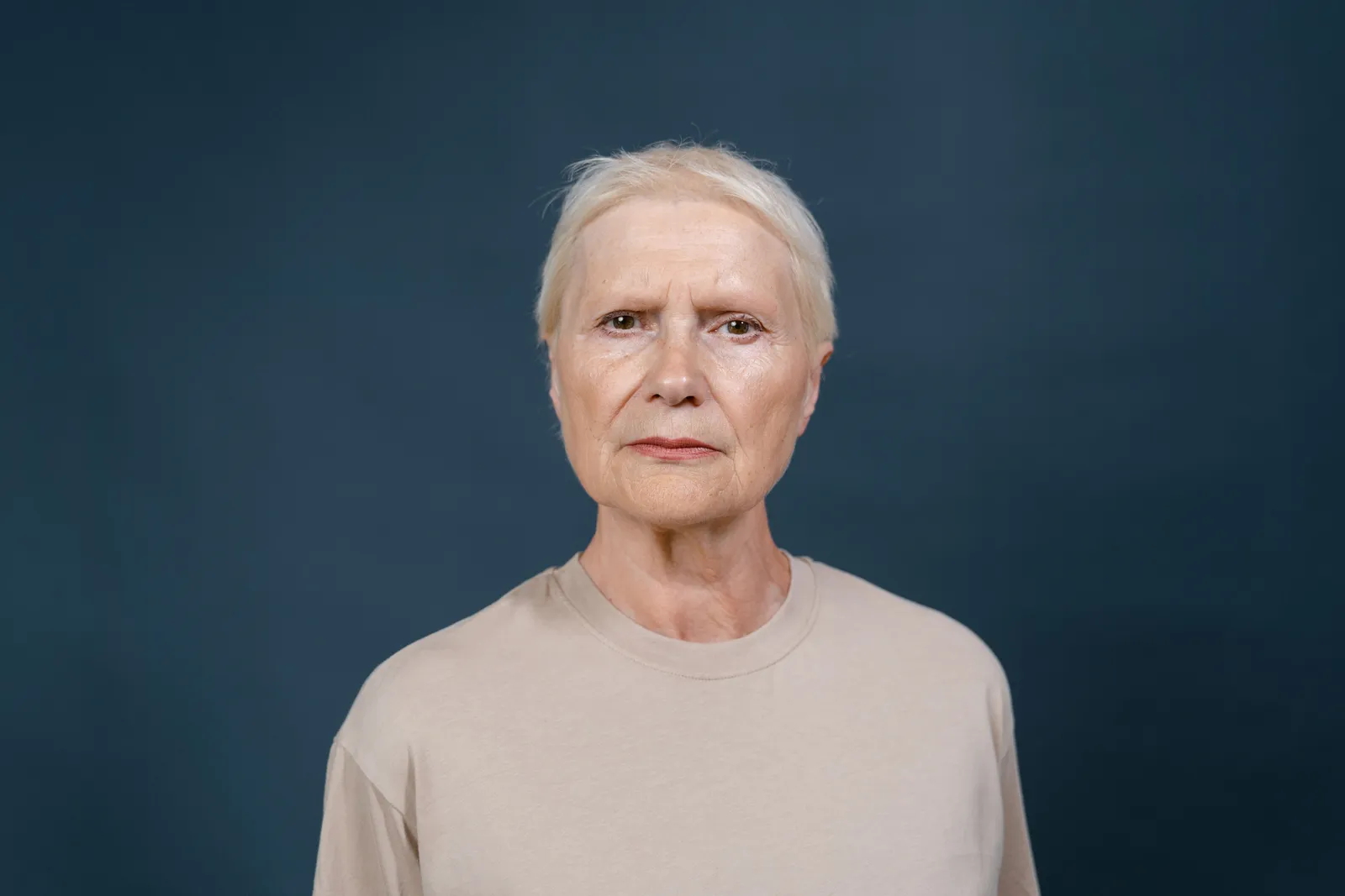 Studio portrait of a senior woman with blonde hair looking confidently at the camera against a blue background