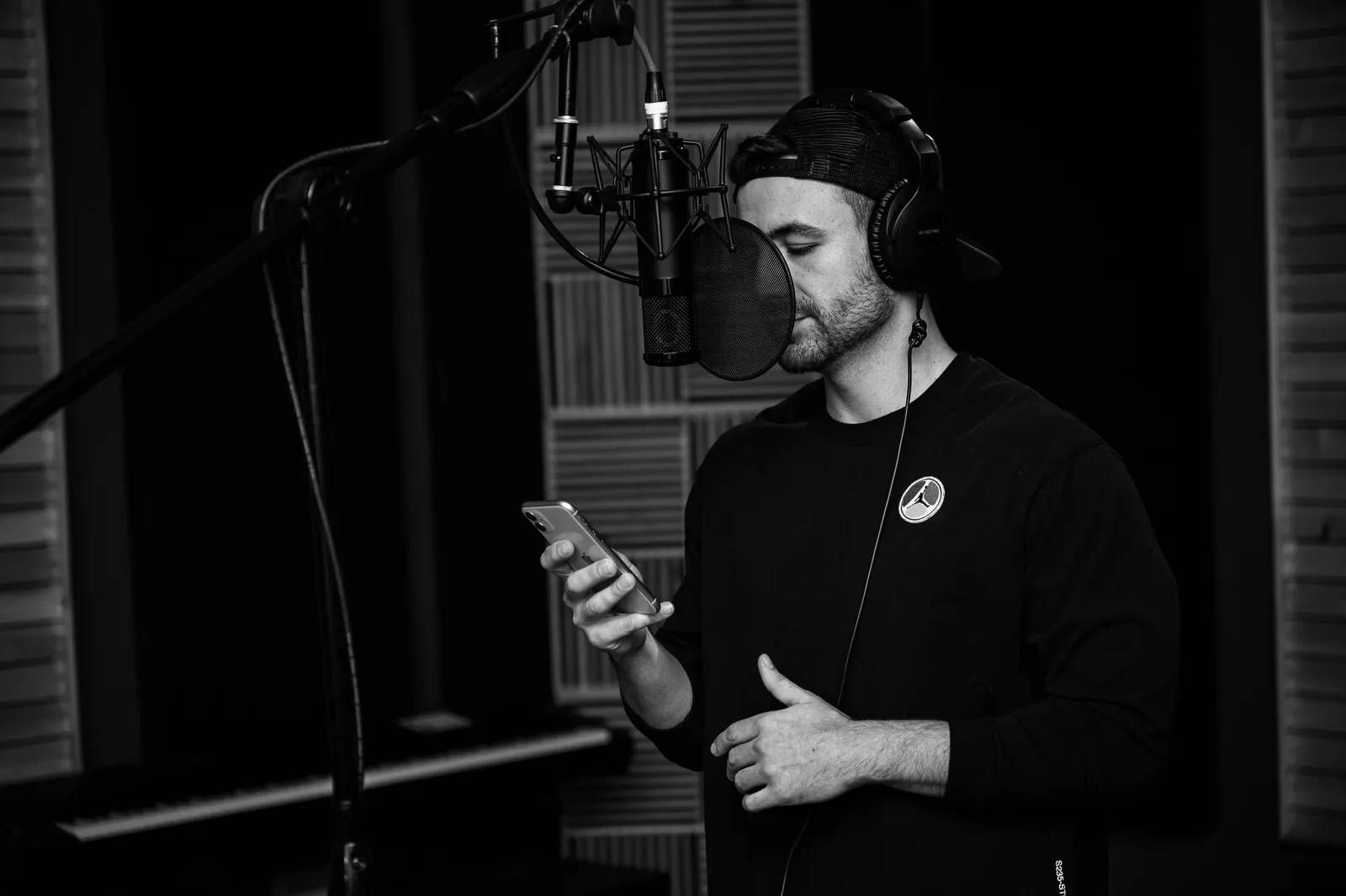 Black and white side view of pensive male artist in casual clothing and headphones reading information on internet while