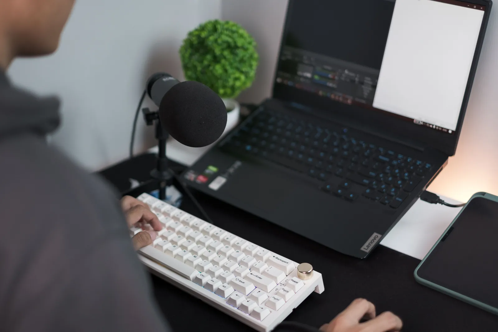 A person at a desk with a laptop, microphone, and keyboard in a modern setup