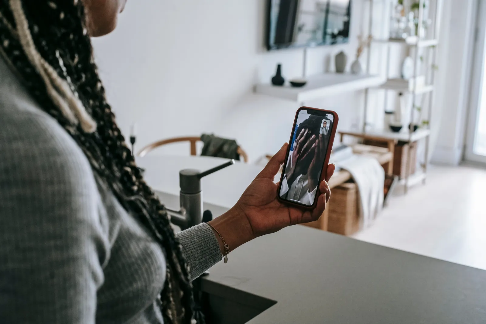 Crop unrecognizable lady with long braids having video call on mobile phone with upset boyfriend covering face with hands