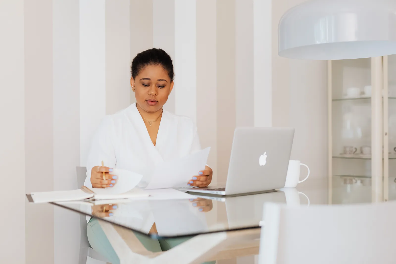 Businesswoman in a modern office, reviewing documents at a glass desk with a laptop