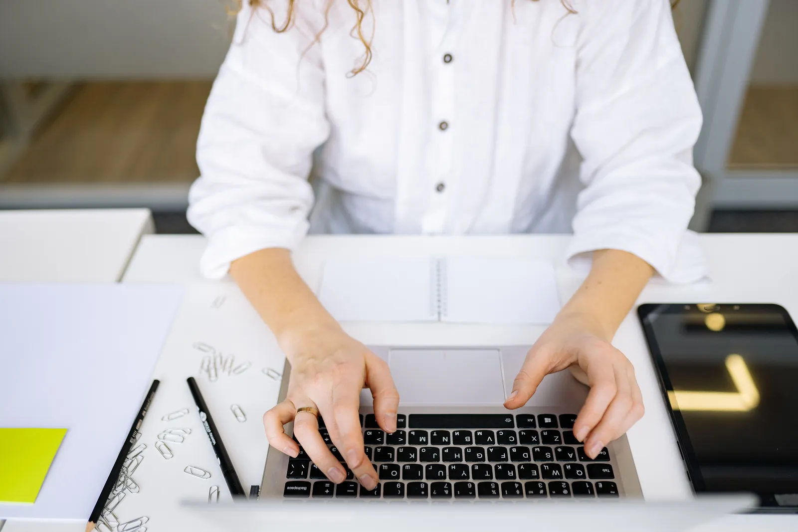 Close-up of woman's hands typing on laptop keyboard in bright, modern office space. Ideal for work and technology themes