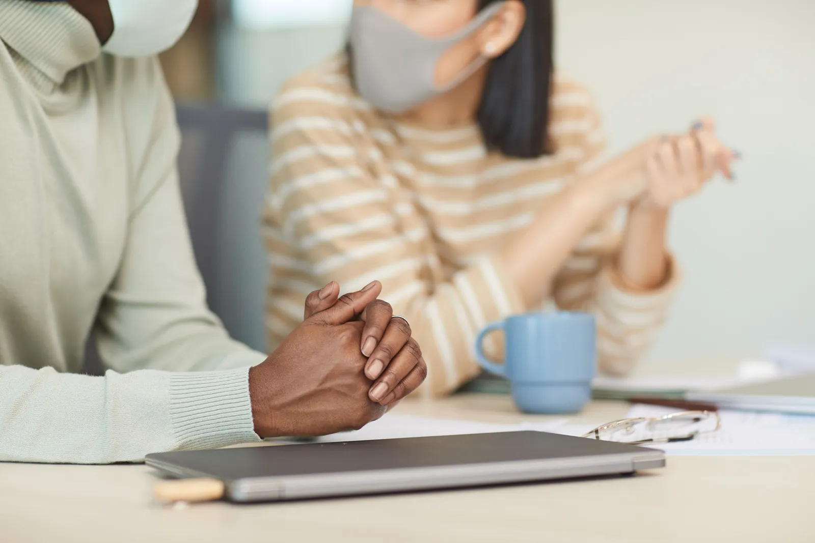 Two colleagues wearing face masks, sitting and discussing work at a desk in a modern office setting