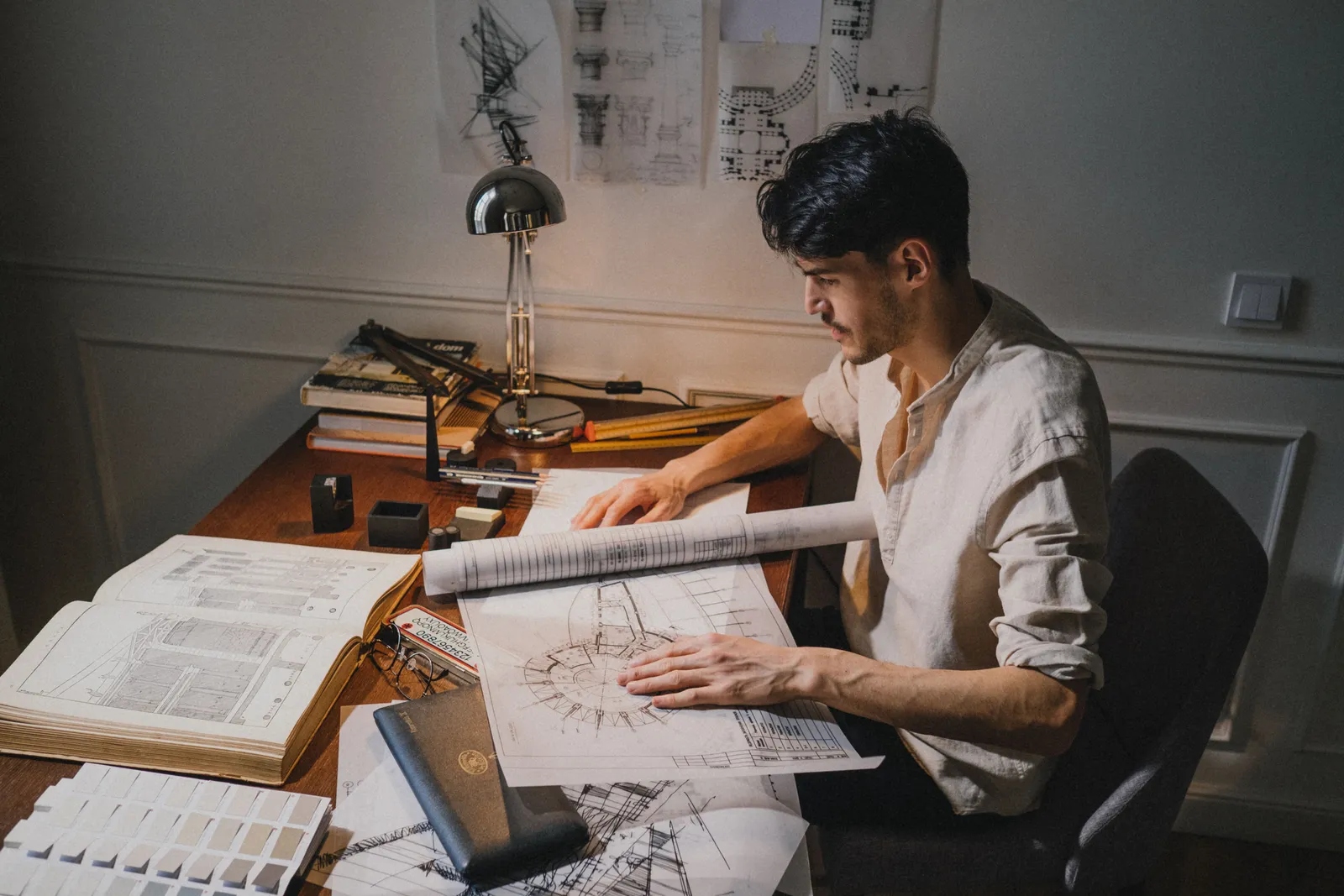 Young architect at a desk working on blueprint designs under lamp light