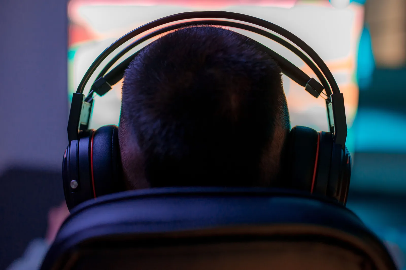 A man wearing headphones intently playing a video game on a computer in a dark room