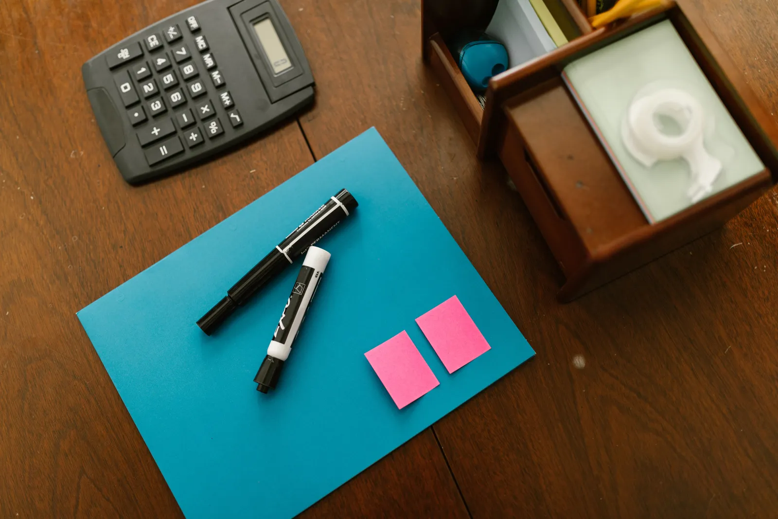 Top view of office supplies including a calculator, markers, and sticky notes on a wooden desk