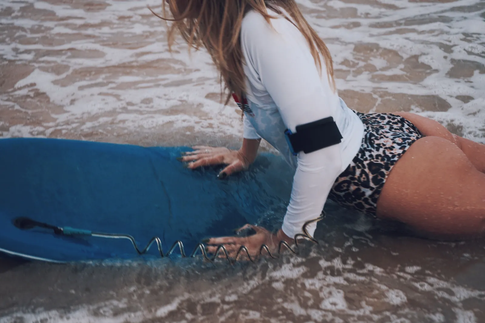 A woman wearing a leopard print swimsuit on the beach, ready to surf with a blue surfboard, showcasing water sports activity