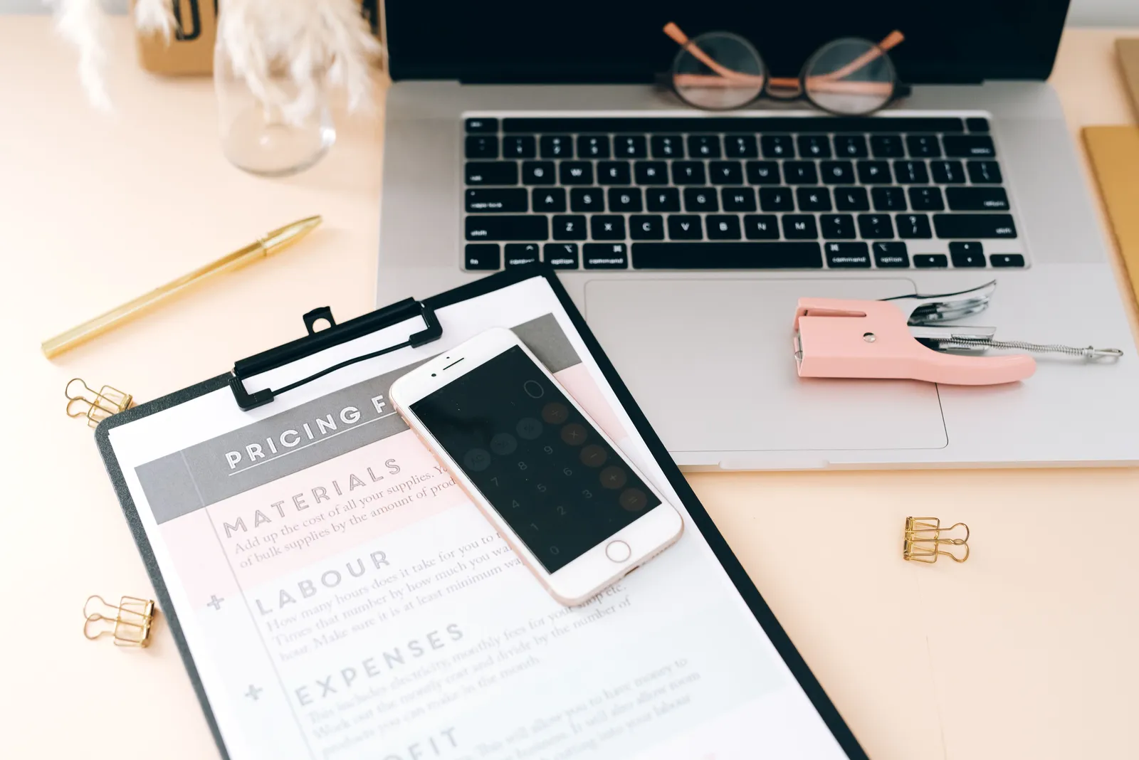 A stylish workspace featuring a laptop, smartphone, clipboard, and stationery essentials
