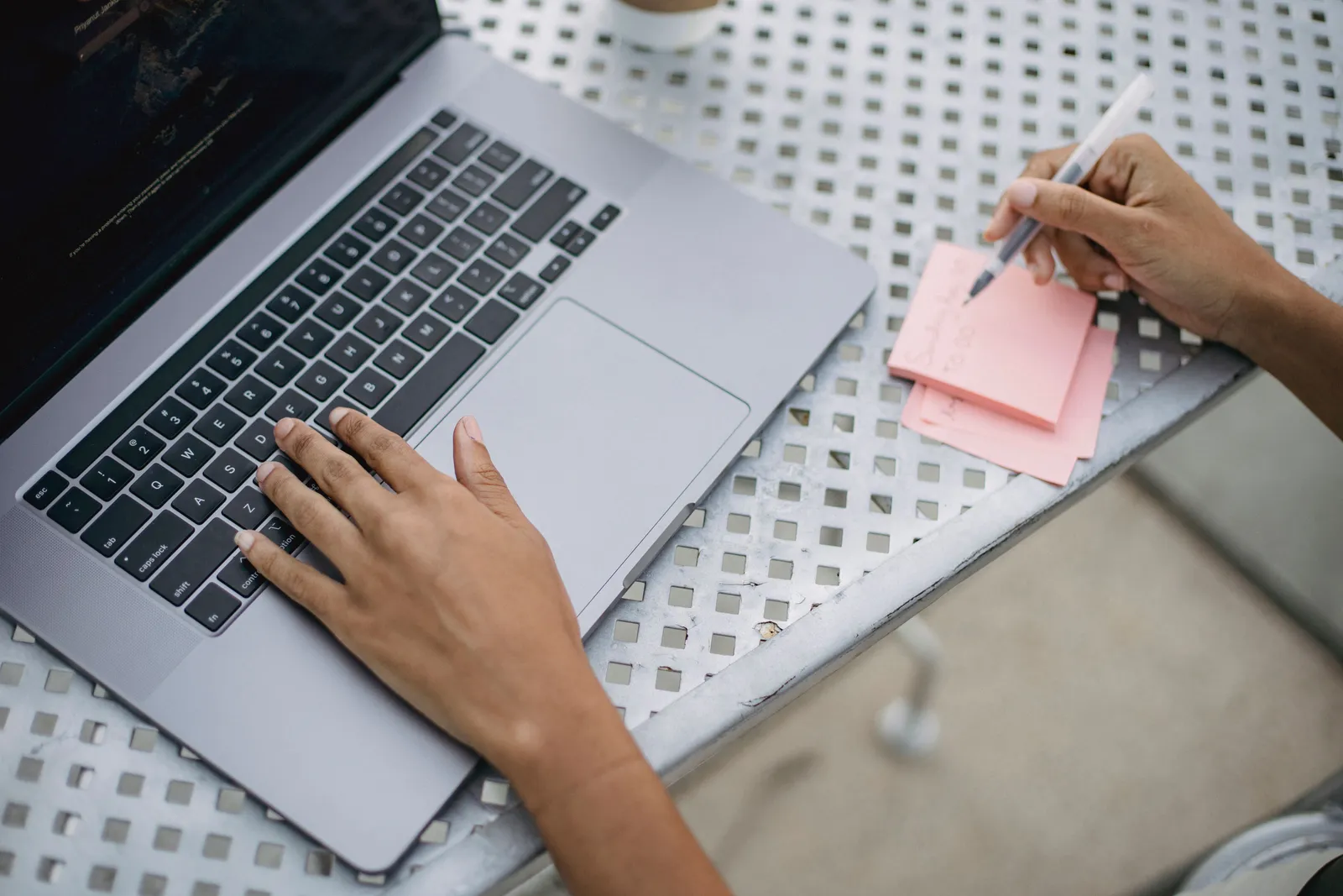 Close-up of a person using a laptop and writing notes at an outdoor workspace