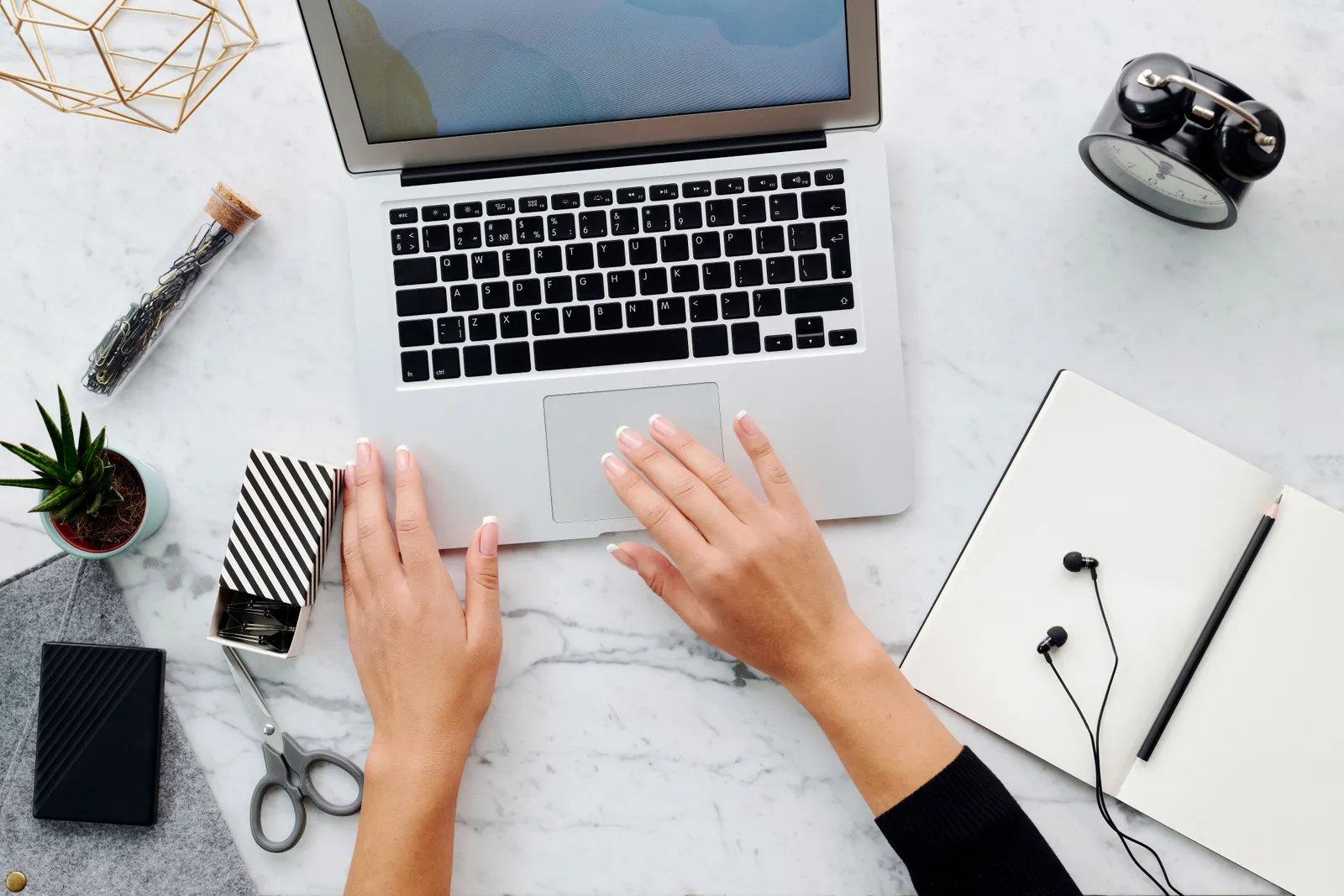 High angle view of hands using laptop on marble desk with office and tech accessories