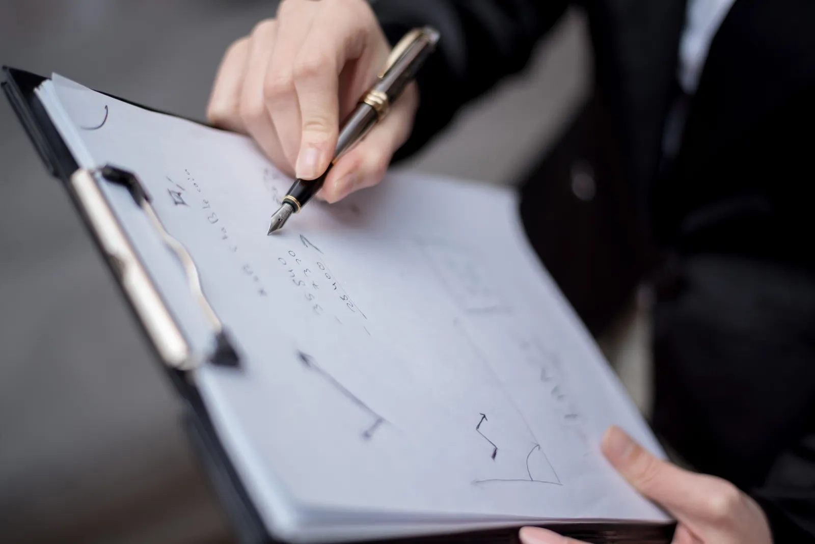 A person writing on a clipboard using a pen, focusing on the hand and paper