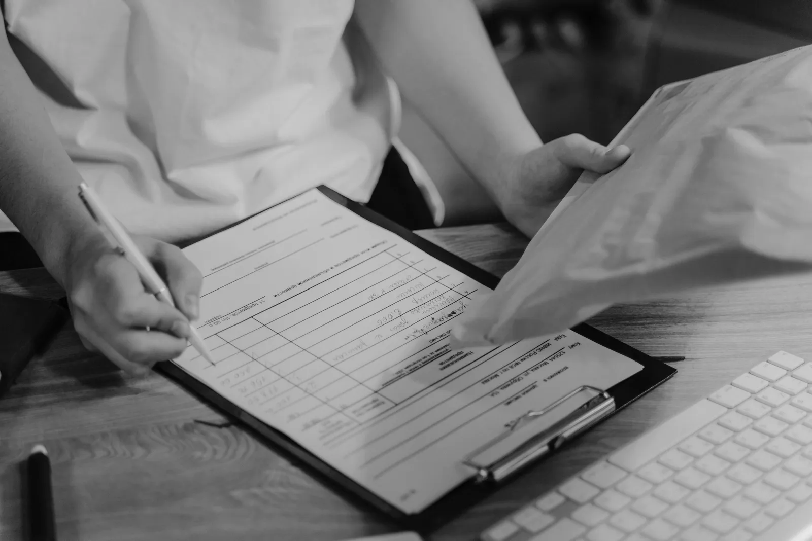 Black-and-white photo of a person writing on a clipboard with a keyboard visible