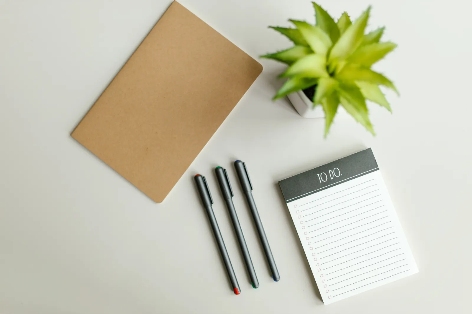 Flat lay of a to-do list, notebook, pens, and succulent on a light gray desk surface
