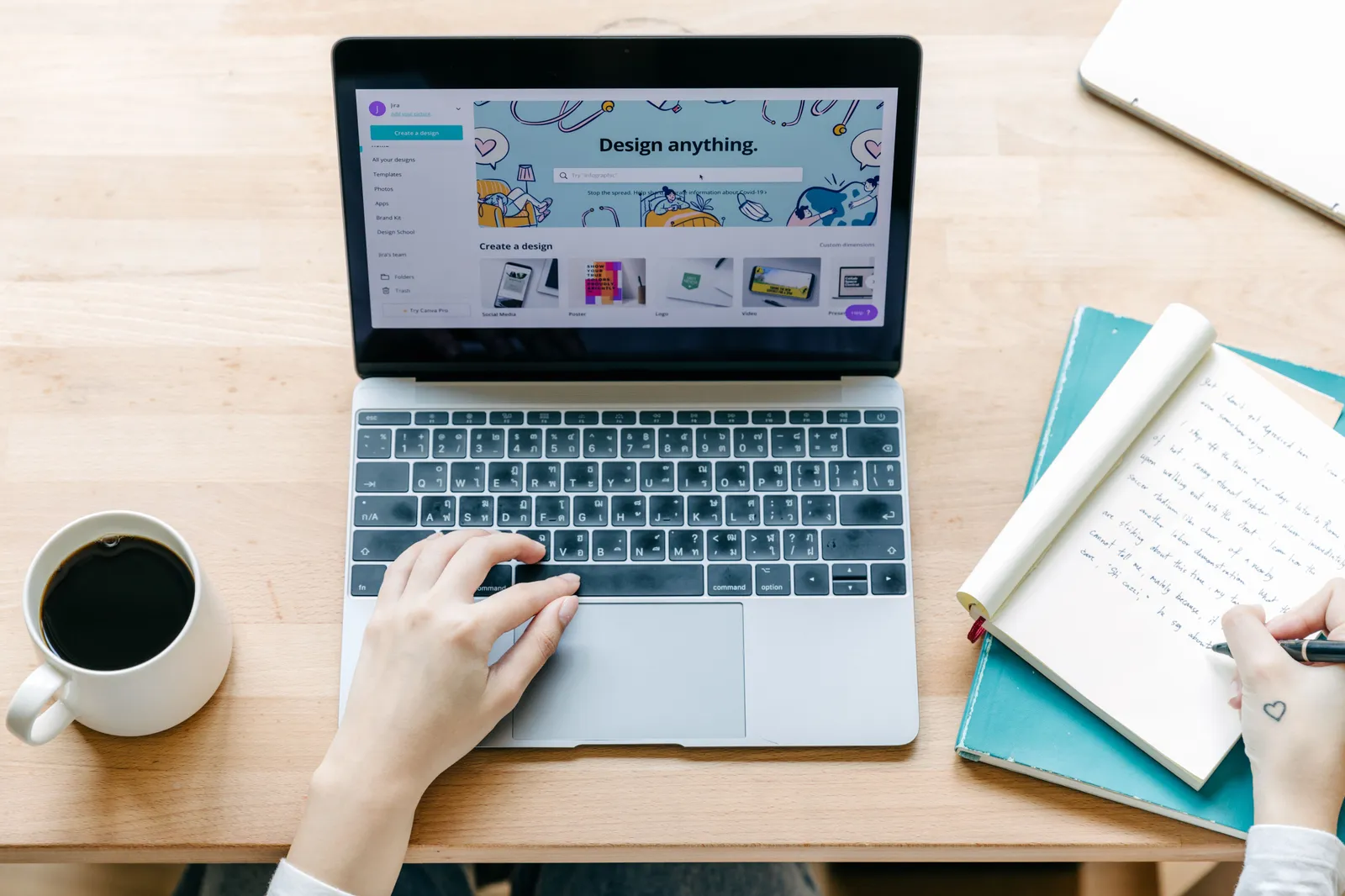 Unrecognizable person typing on laptop and writing notes in notebook while sitting and working on design project in modern