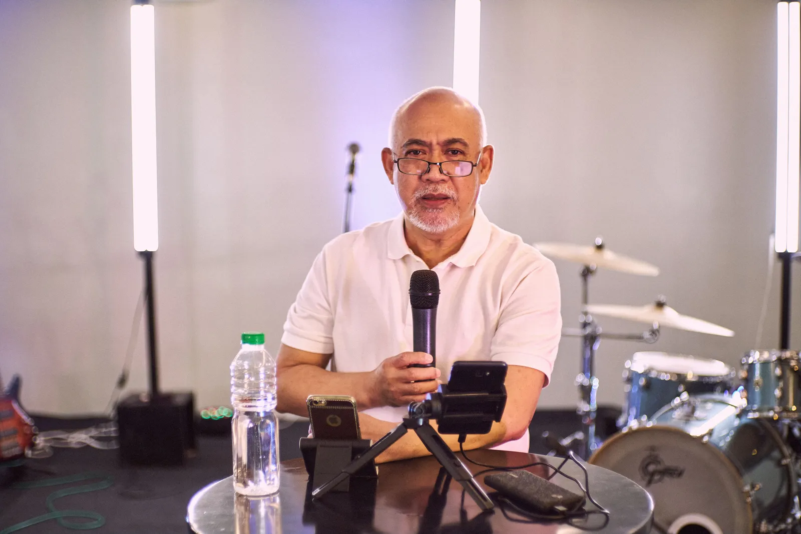Senior man in a studio setting using a microphone with a drum set in the background