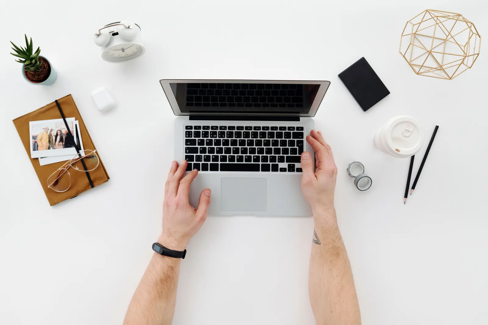 Top view of a minimalist workspace featuring a laptop, office supplies, and a person's hands typing on a laptop