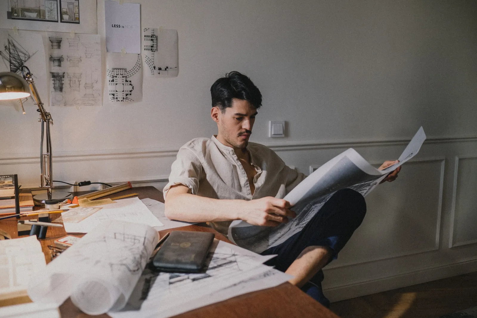 Man reviewing architectural plans at desk in sunlight, displaying concentration and creativity