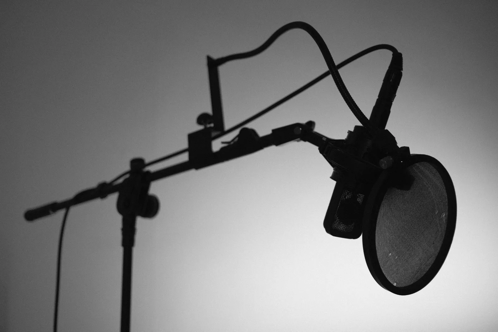 Black and white image of a professional studio microphone with a boom arm and pop filter