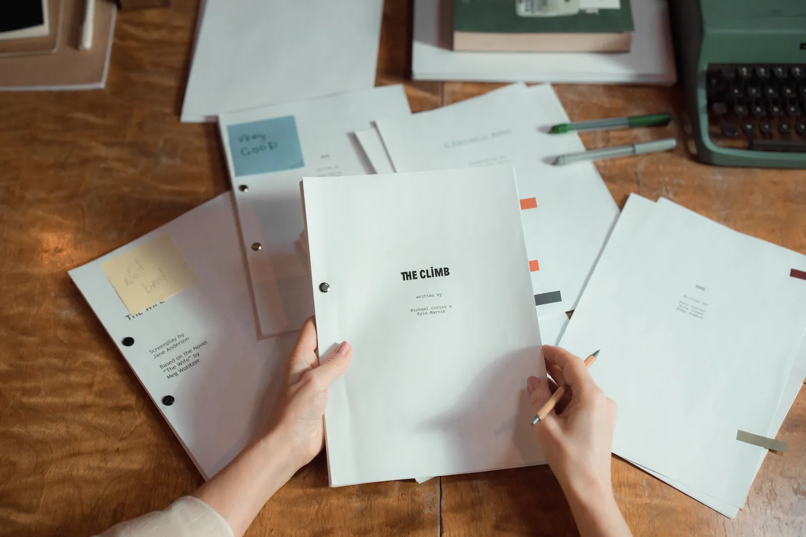 Close-up of hands holding script pages on a wooden desk with a typewriter