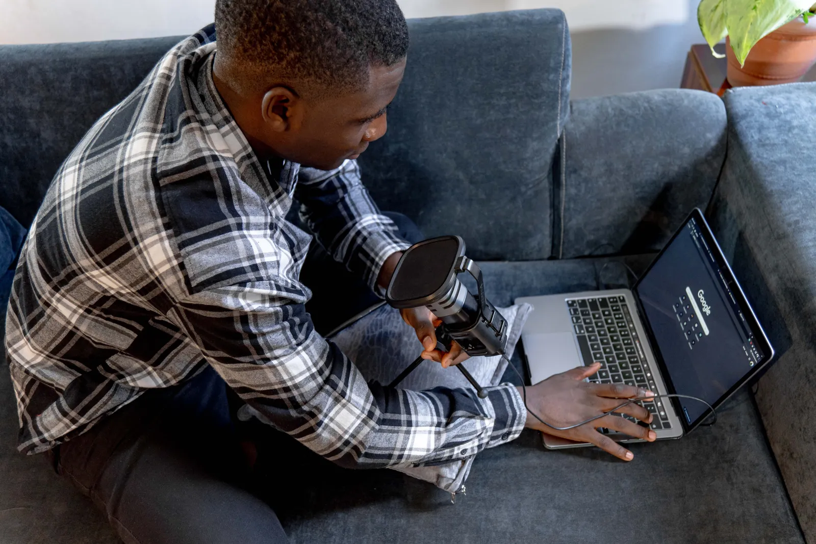 A young man holding a microphone and using a laptop on a sofa, indoors setting