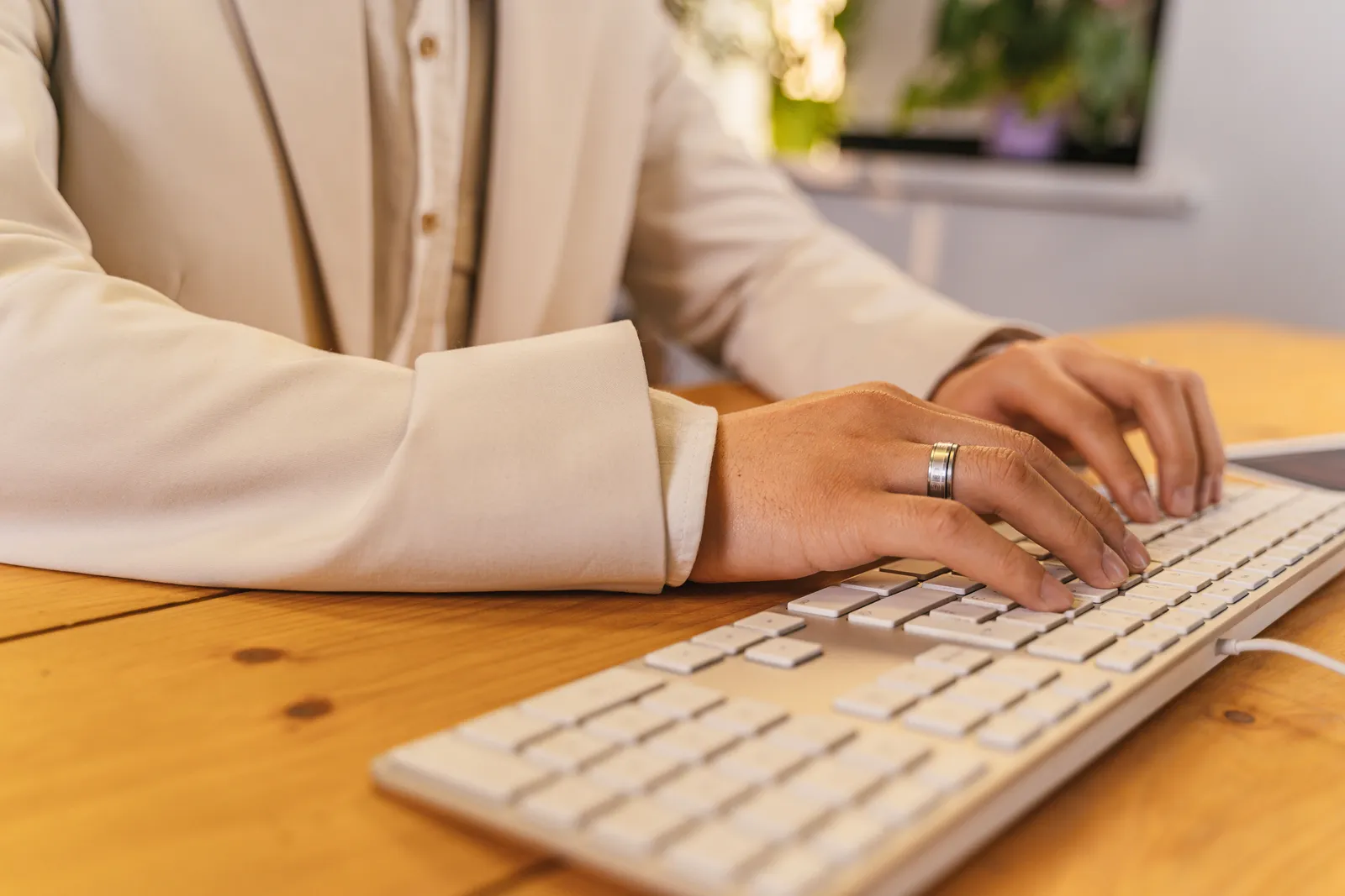 Close-up of a professional typing on a keyboard at a desk, wearing a suit jacket