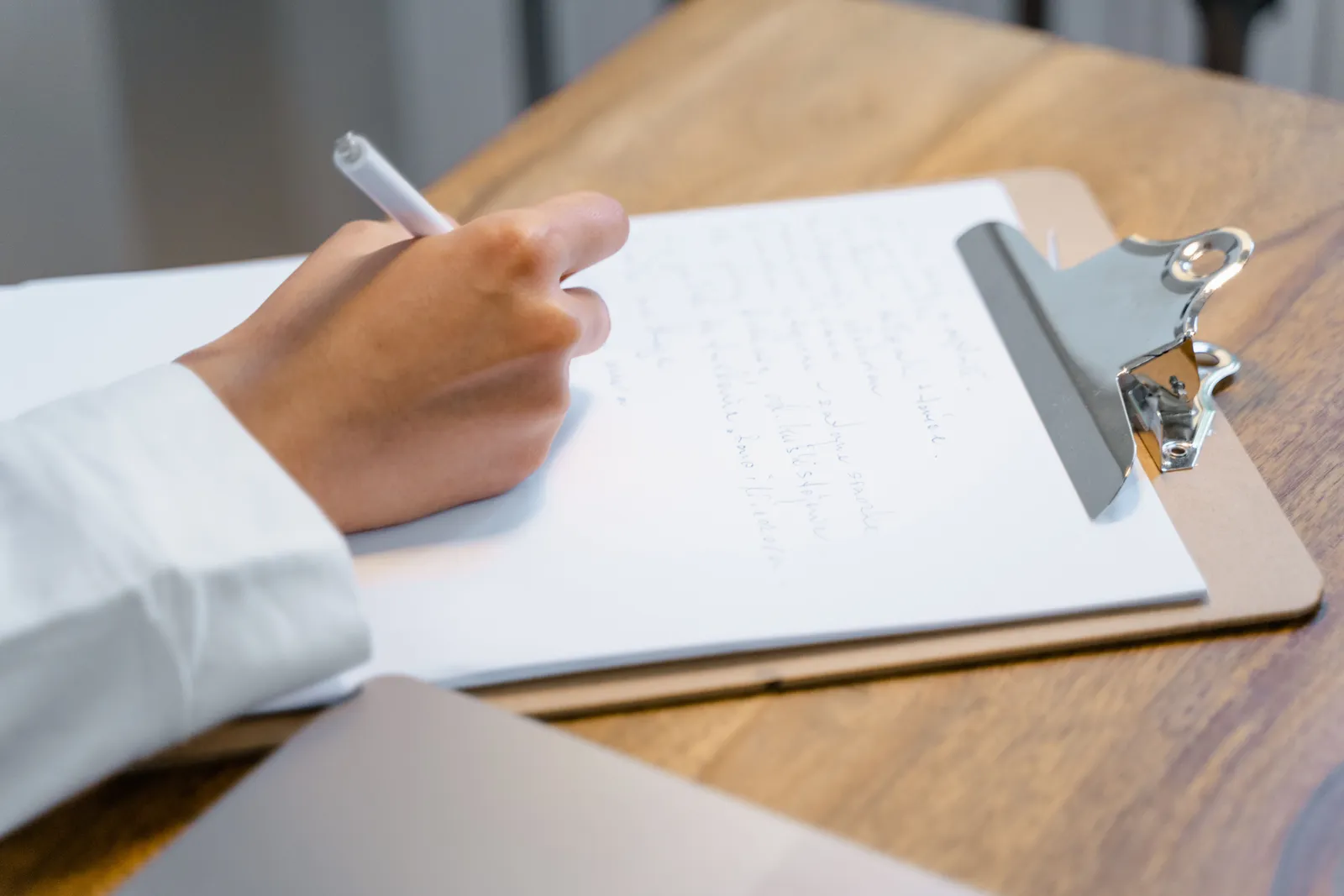 A close-up of a person's hand writing on a clipboard on a wooden table, displaying focus and concentration