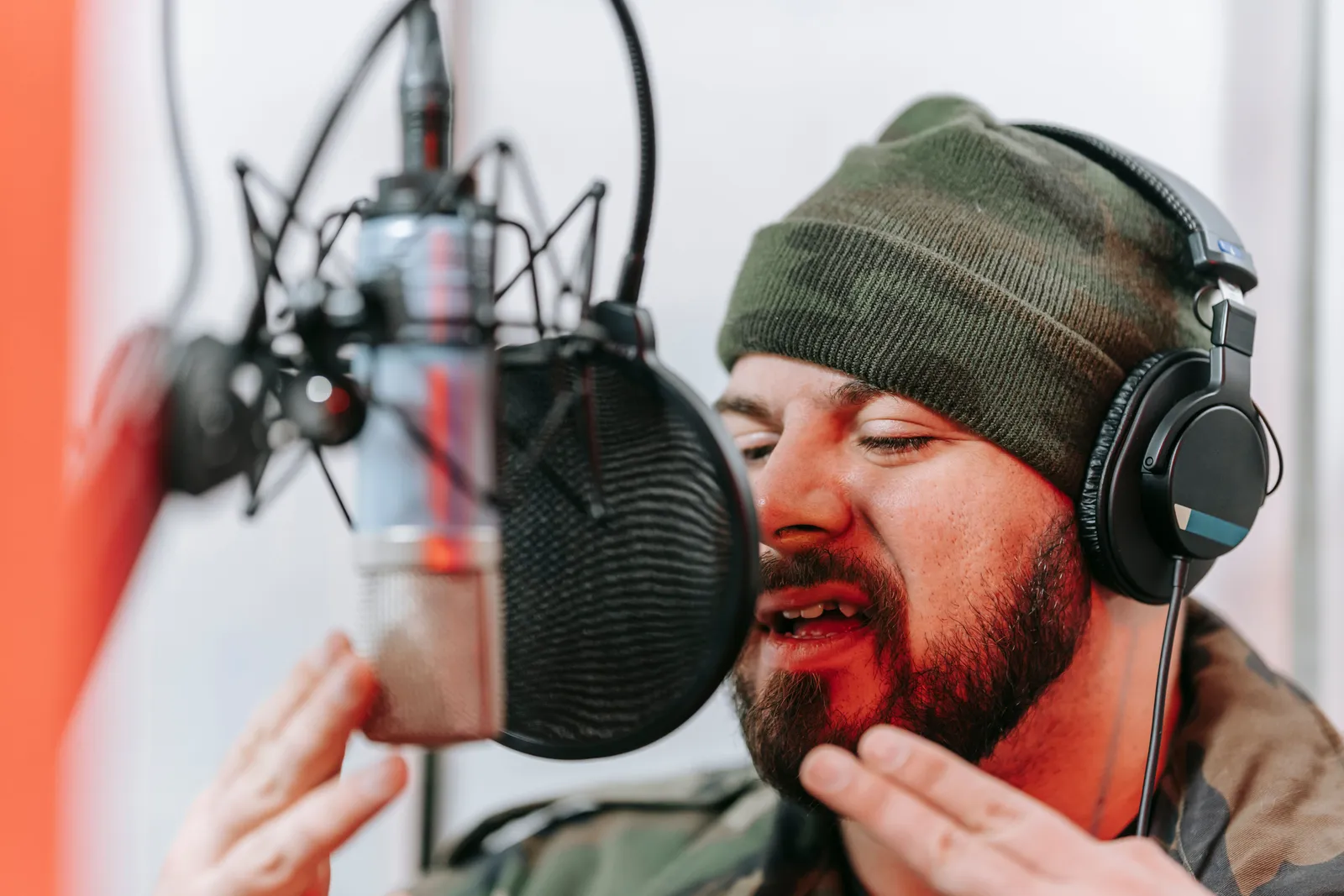 A bearded man wearing headphones sings passionately into a condenser microphone