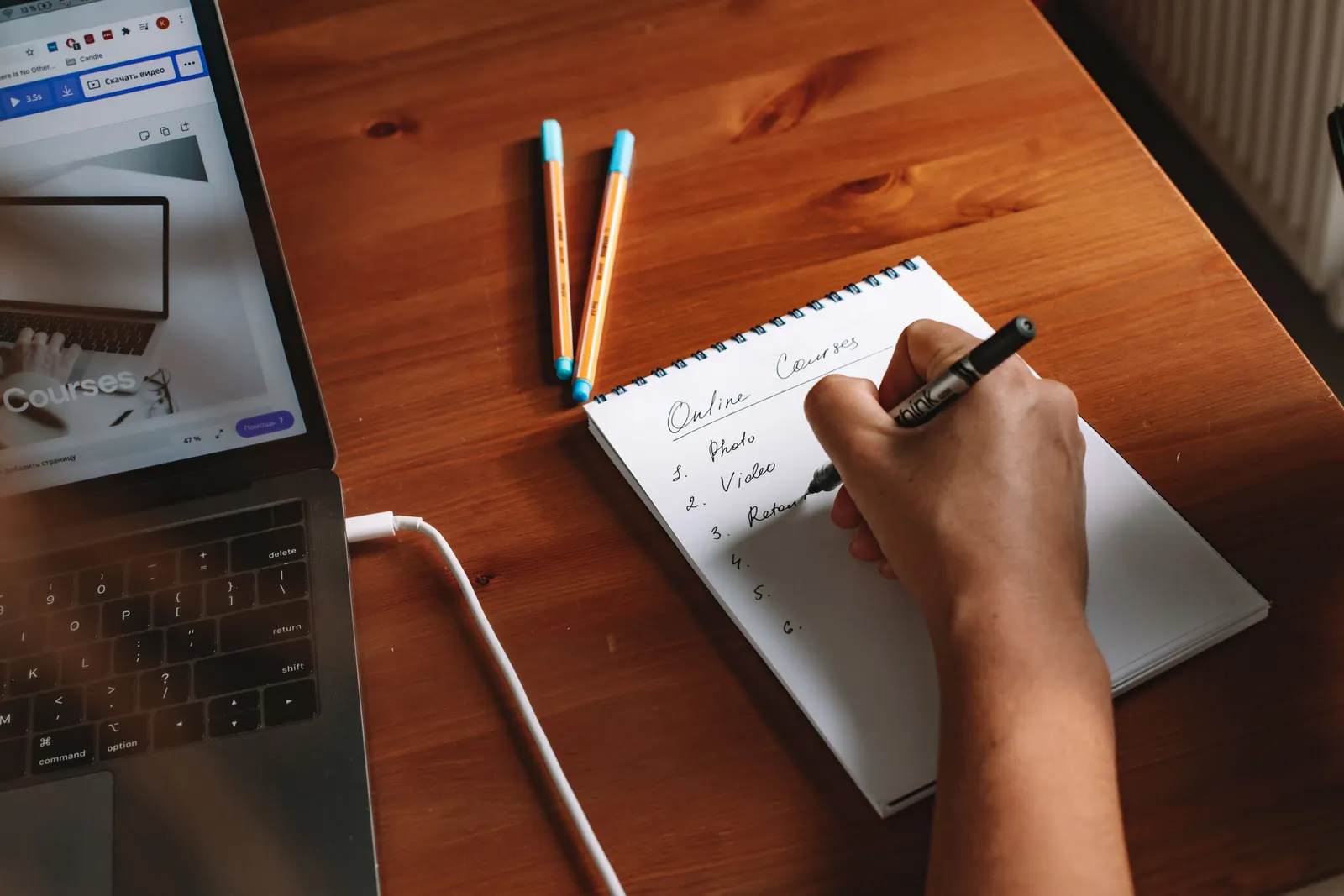 Photo of a person writing a list of online courses on a notepad next to a laptop