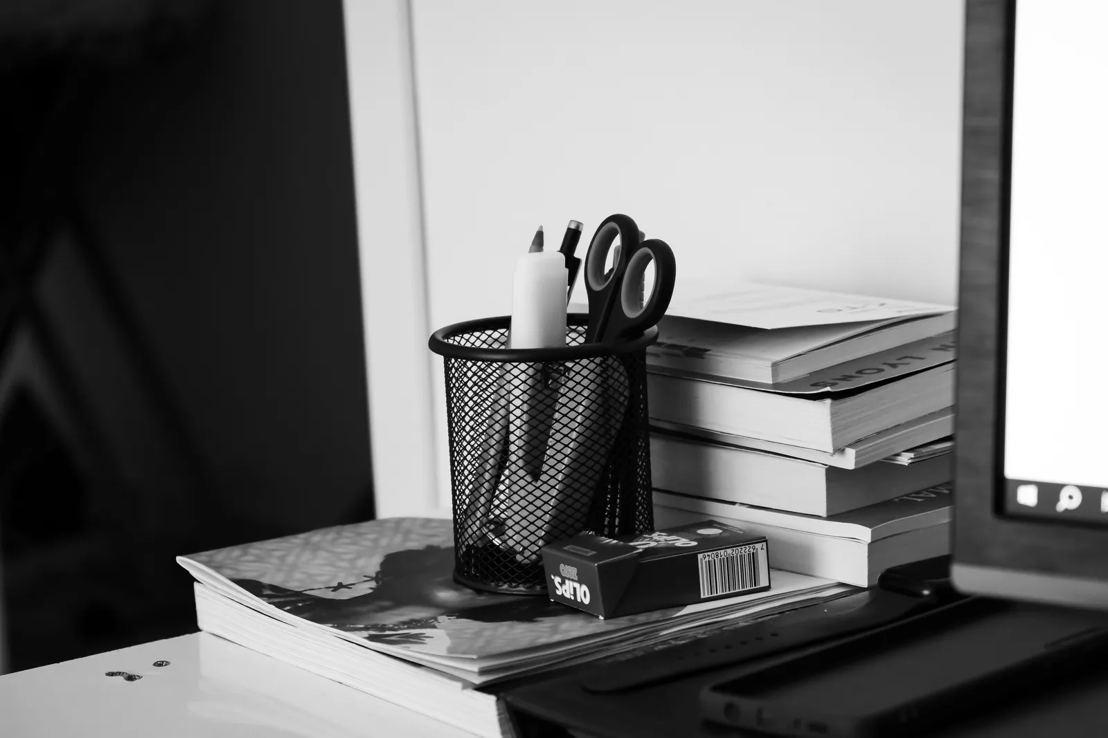 A black and white photo of a home office desk with books, stationery, and a laptop